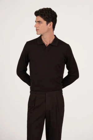A man wearing a dark, long-sleeve polo shirt and pleated trousers poses against a neutral backdrop, looking to the side in a studio shot.