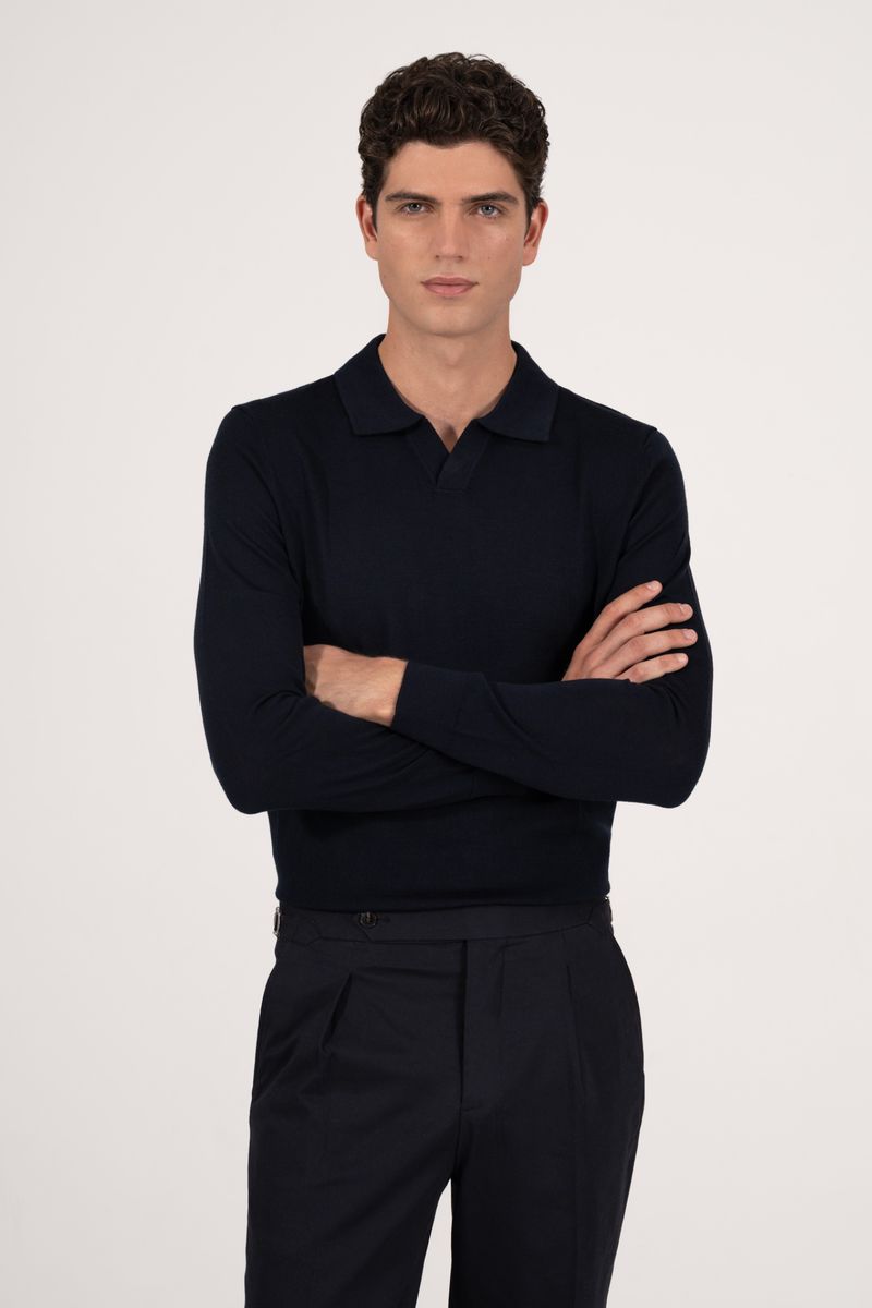 Adult male in dark-blue polo shirt with long sleeves and black pants posing against a neutral background with his arms crossed.