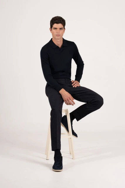 A fair-skinned adult male sits on a white stool wearing a dark navy long-sleeve polo shirt with matching pants and shoes in a studio.