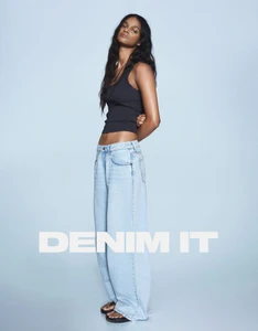 Model wearing a black tank top and light blue denim jeans against a plain blue background for Bershka DENIM IT campaign
