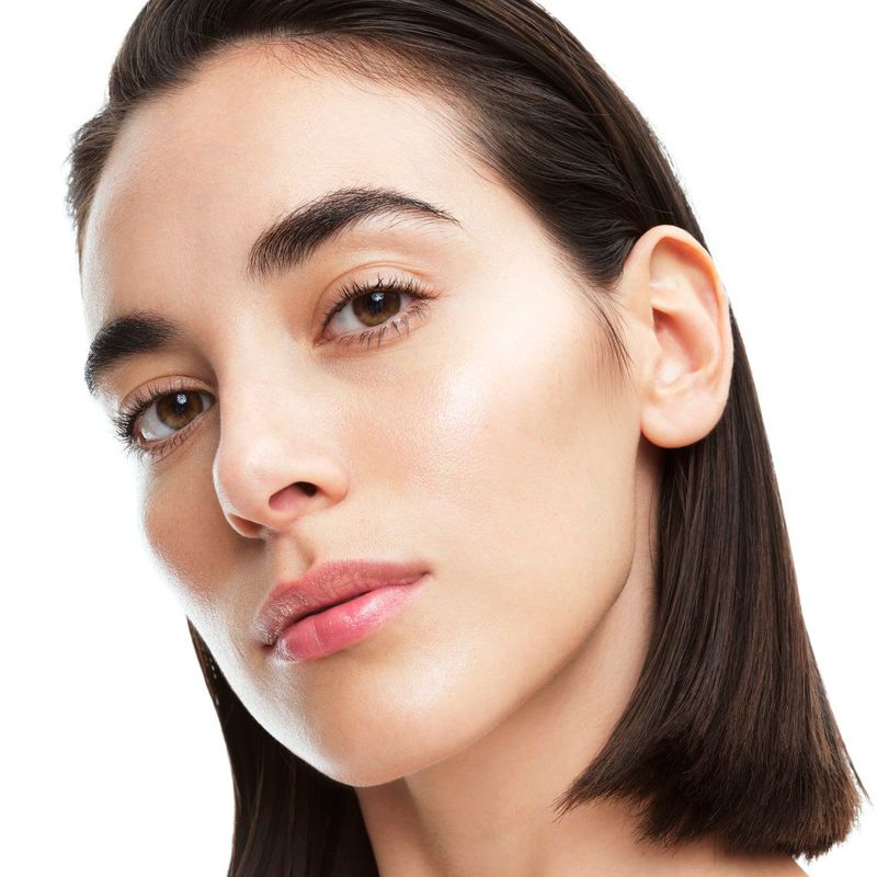 Close-up portrait of a young adult woman with fair skin, brown eyes, and short dark brown hair, against a white background. Beauty shot.