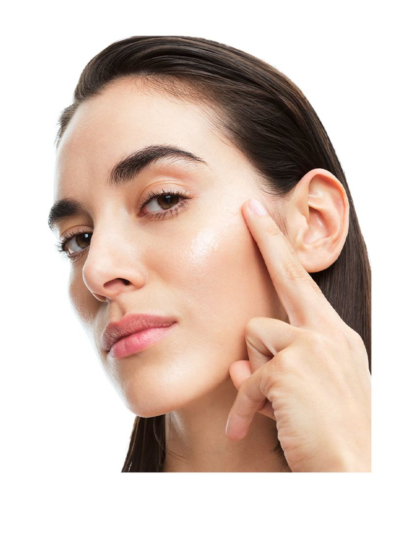Close-up studio shot of an adult woman with brown hair touching her face, showcasing a beauty or skincare product against a white backdrop.