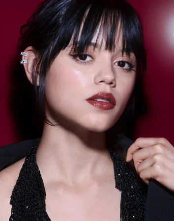 Close-up of a woman with dark hair and glossy lips, wearing a black top, against a red background in soft, diffused lighting.