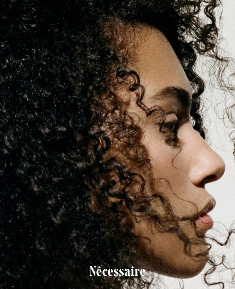 Profile portrait of a Black woman with textured curly hair and a subtle nose ring against a white background for N cessaire hair care campaign