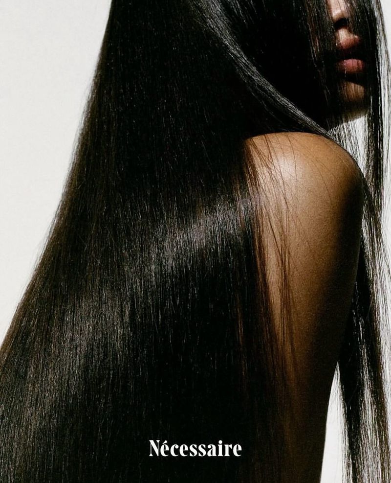 Close-up portrait of a Black woman with long, sleek dark hair cascading down her back against a white background with product text.