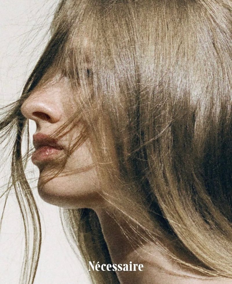 Close-up profile portrait of a young adult female with blonde hair covering her face against a clean, light background.