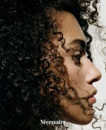 Profile portrait of a Black woman with textured curly hair and a subtle nose ring against a white background for N cessaire hair care campaign