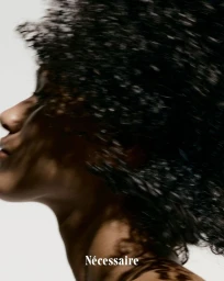 Close-up profile of a black woman with dark curly hair in motion against a plain white background for the Necessaire hair serum campaign.