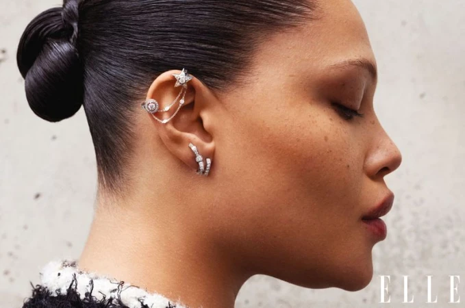 Close-up of an adult female model wearing jewelry, including ear cuffs and earrings, with her hair pulled back and wearing makeup.