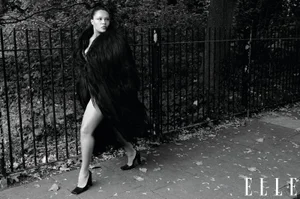Model Alva Claire wearing a dark textured coat and heels walking past a metal fence for Elle UK shot by Fabien Montique