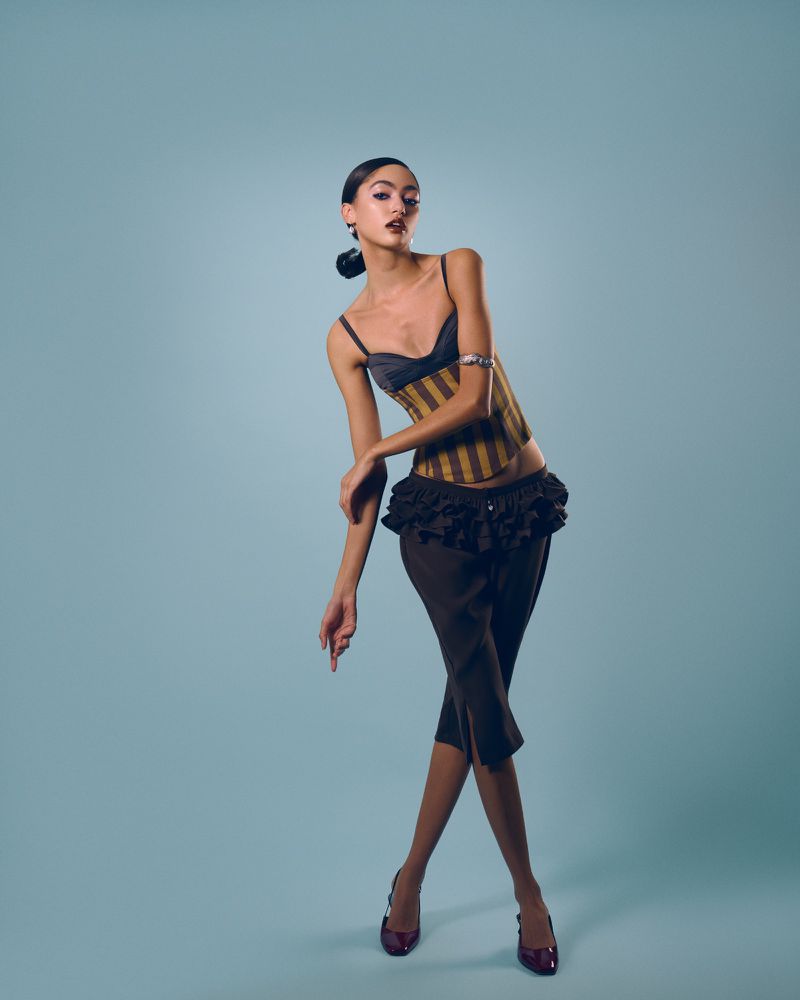 Fashion portrait of a young woman posing in a corset top and dark pants on a light blue background in a photo studio with medium shot.