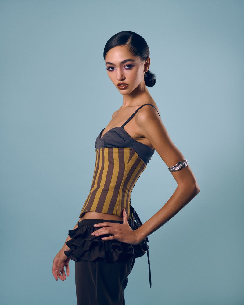 Model in striped corset top and ruffled pants posing against a plain light blue studio background