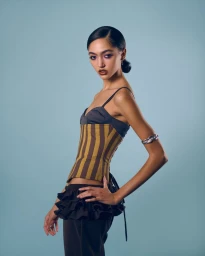 Model in striped corset top and ruffled pants posing against a plain light blue studio background