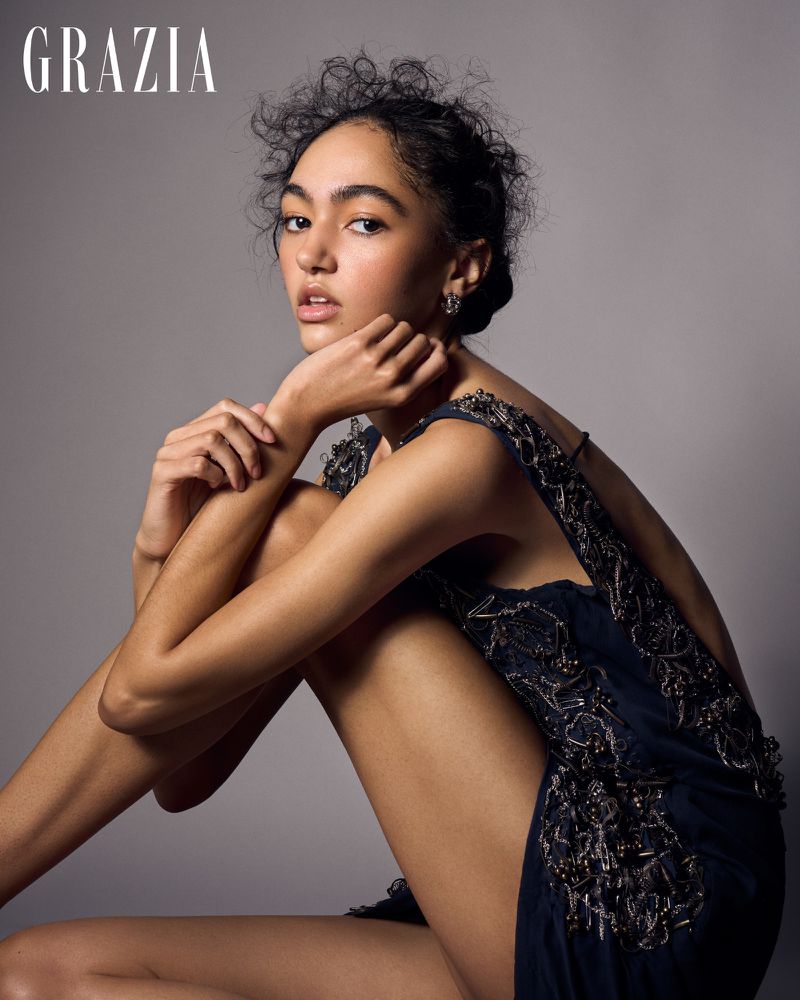 Model with dark curly hair wearing an embellished navy dress against a neutral grey studio background for Grazia Bulgaria.