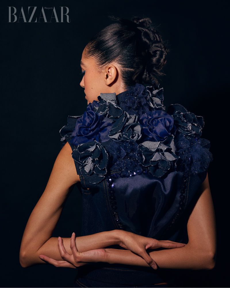 Fashion shot: woman in dark blue top with floral details. Dark background, fashion editorial style, posed back view, studio lighting.