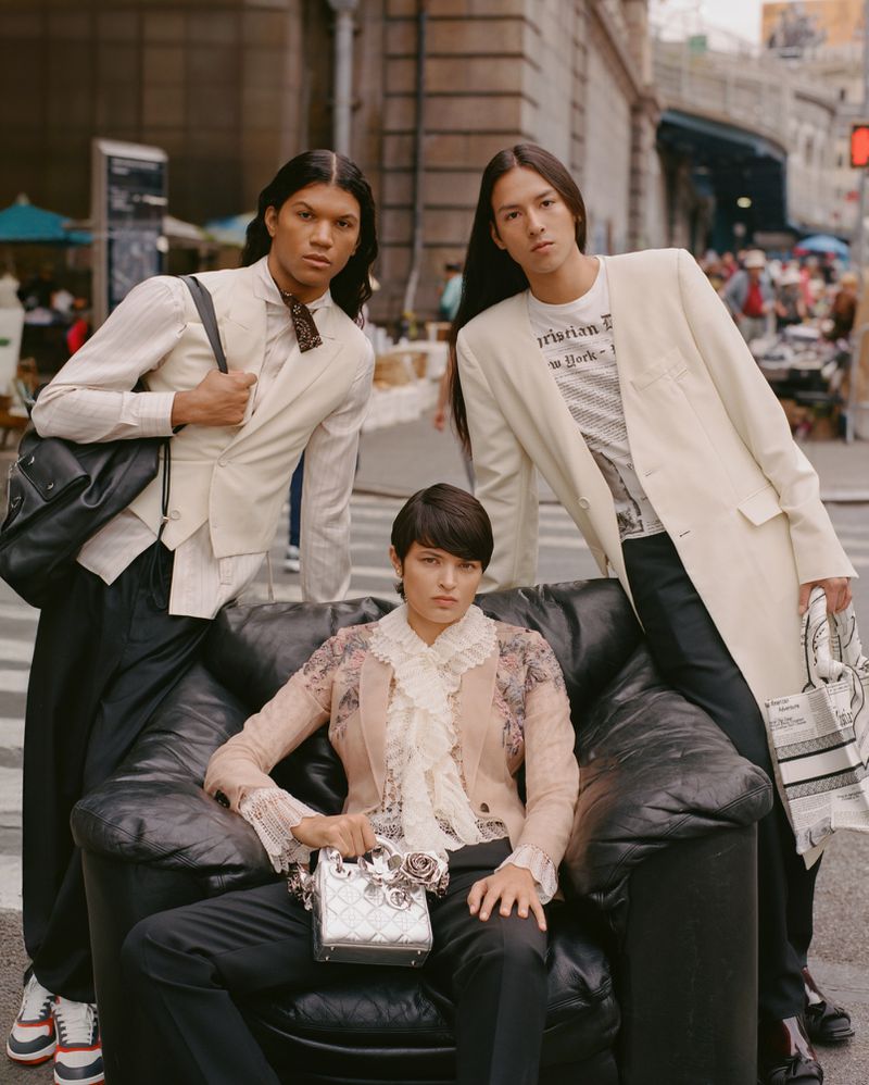 Three fashion models posing around a black leather armchair on an outdoor city street, styled in cream tailoring and lace.