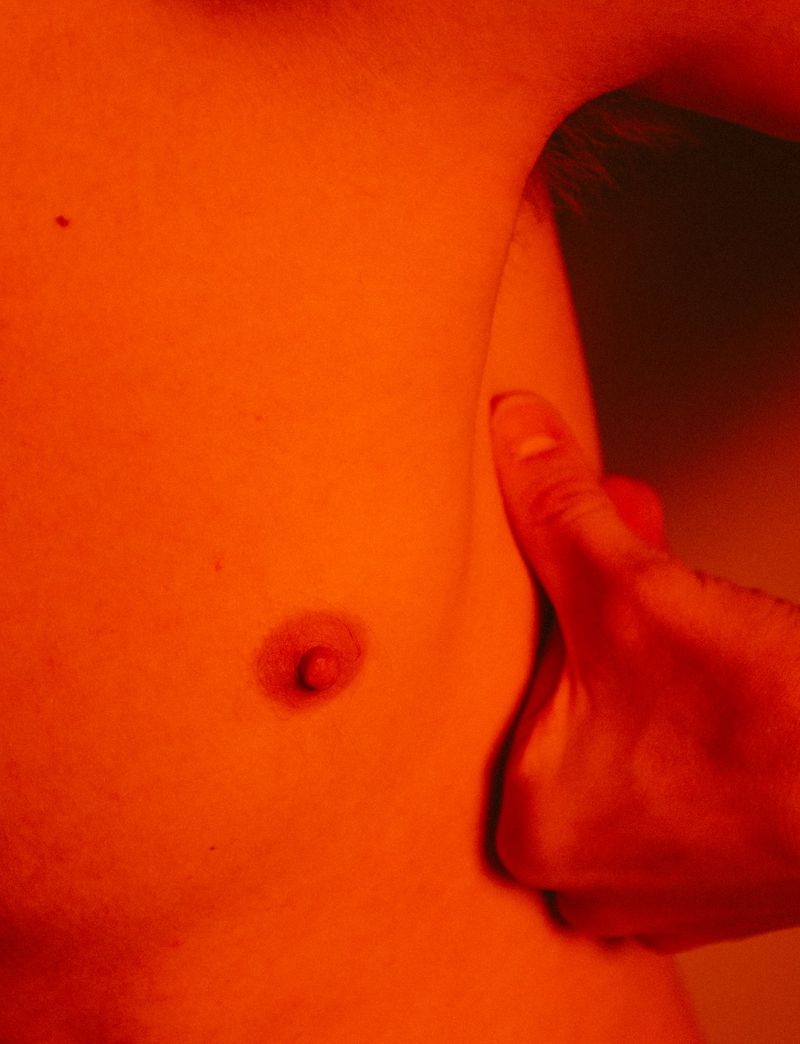 Close-up of a male torso showing the chest and part of an arm, under red lighting emphasizing skin texture, creating a dramatic effect.