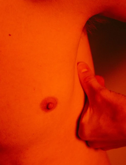 Close-up of a male torso showing the chest and part of an arm, under red lighting emphasizing skin texture, creating a dramatic effect.
