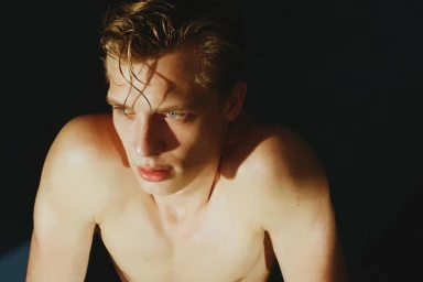 Close-up portrait of a shirtless young man with wet hair under dramatic lighting against a dark background.