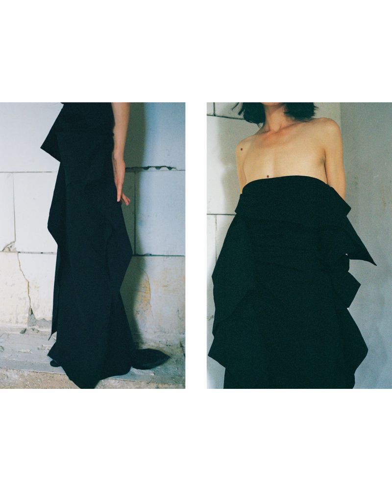 Model Akti Konstantinou in structured black strapless garment against a weathered wall for Crosscurrent project In Waiting