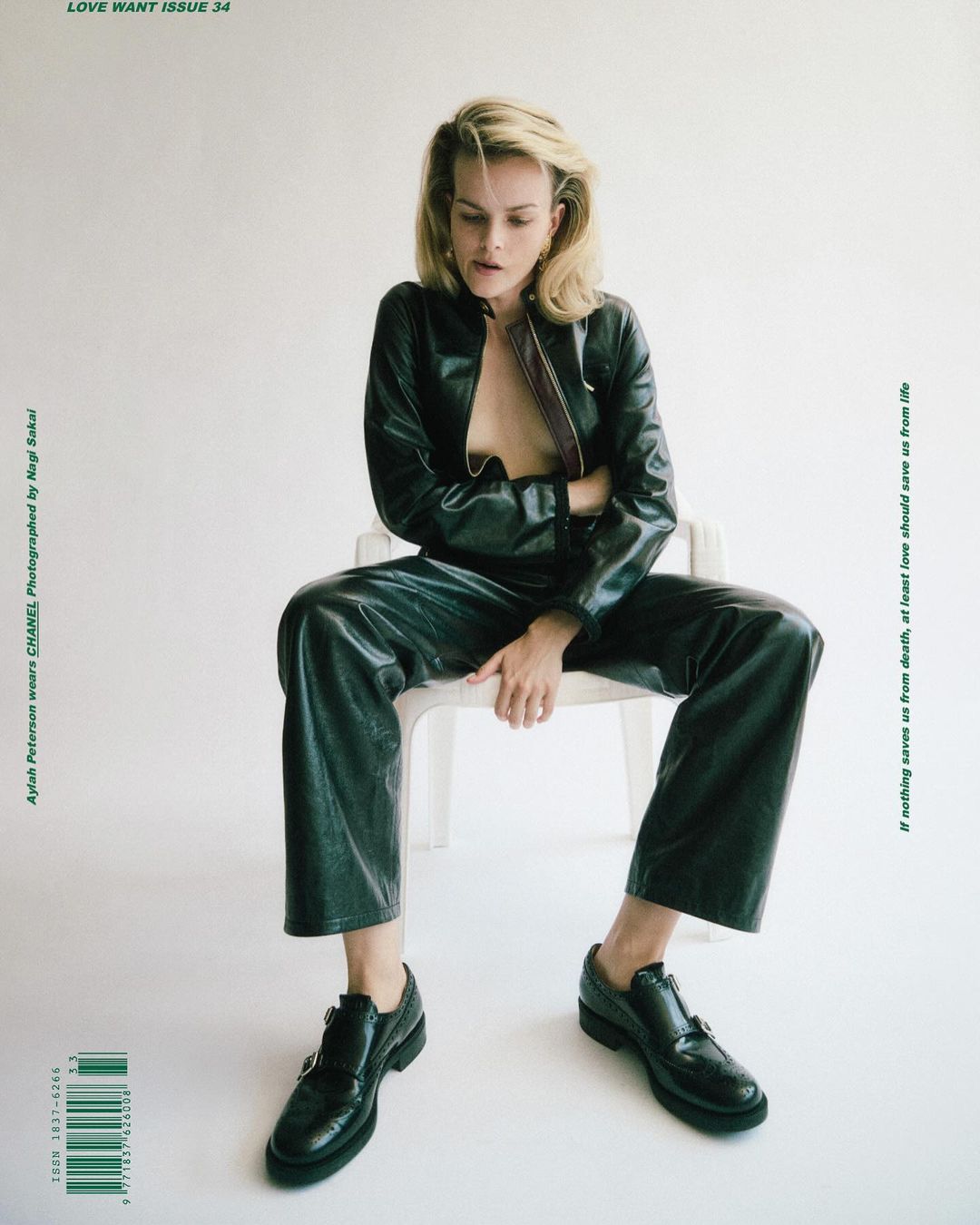 Sylvia Peterson sits on a white chair wearing a black leather jacket and pants with black shoes in a fashion editorial shot.