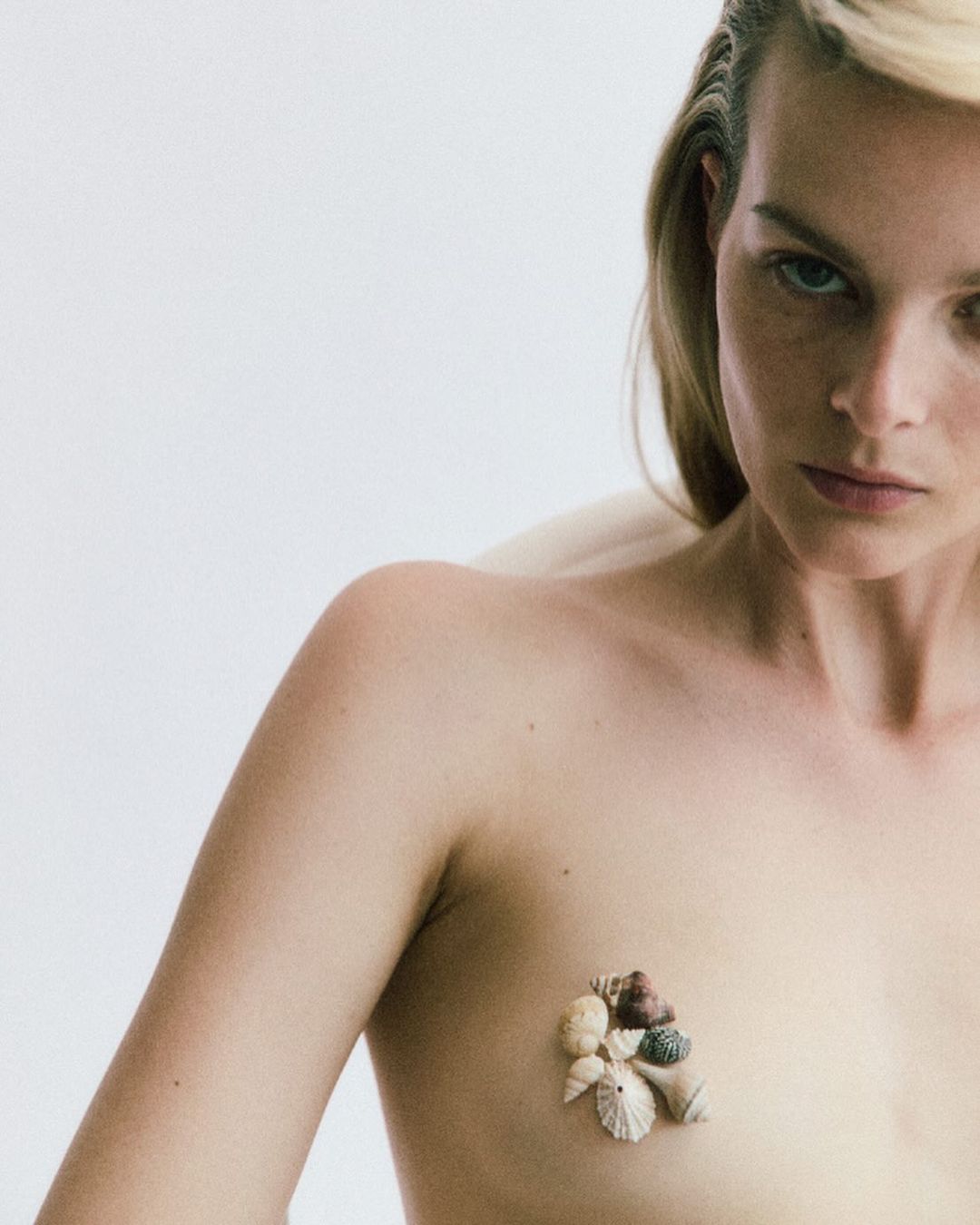 Adult female portrait in a photo studio. Seashells adorn the model's chest against a stark white background, captured in soft, diffused lighting.