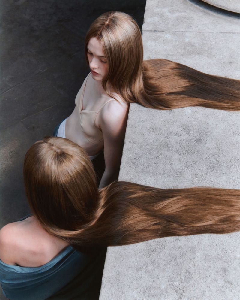 High-angle shot of two women with extremely long brown hair draped across a flat concrete ledge.