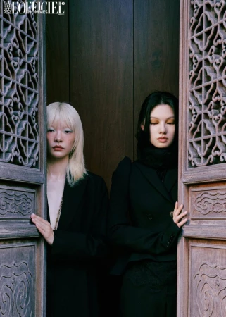 Two models in tailored black jackets standing between open ornate carved wooden lattice doors.