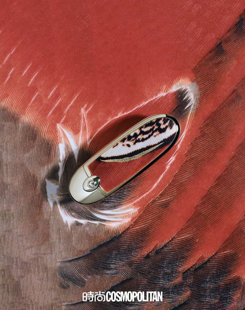 Close-up of an ornate, decorative golden safety pin on a background featuring a feather pattern with tones of brown and orange.