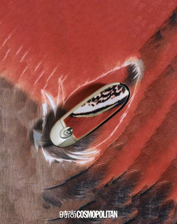 Close-up of an ornate, decorative golden safety pin on a background featuring a feather pattern with tones of brown and orange.