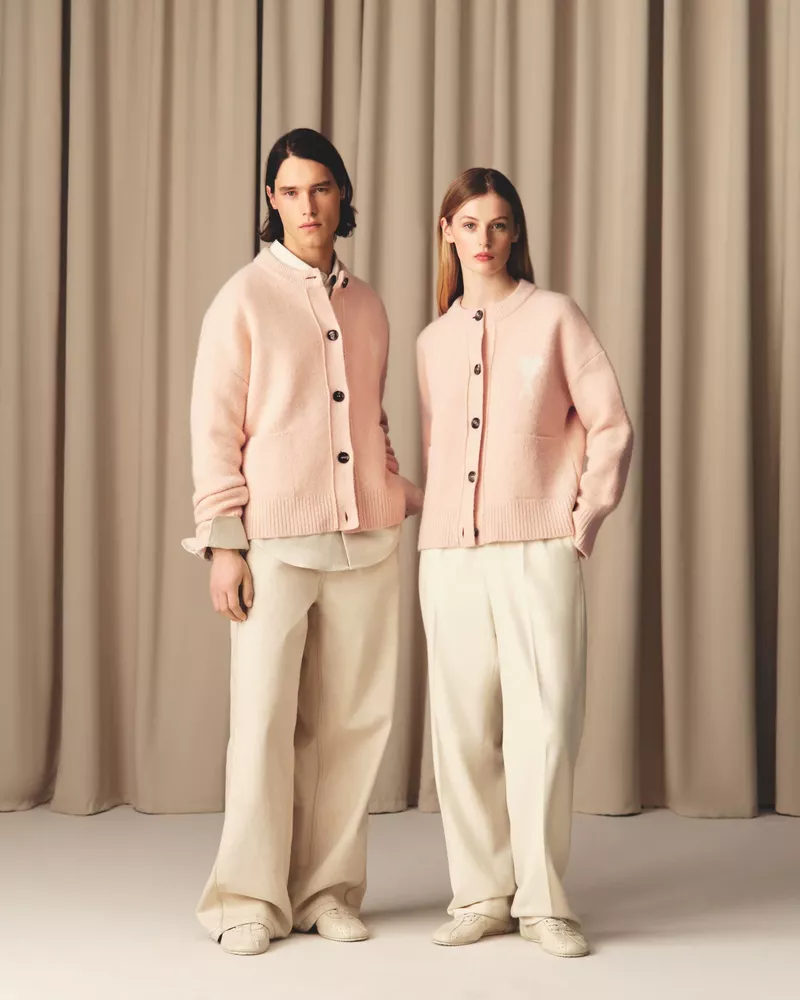 Two models in a neutral studio setting showcase fashion apparel: pale pink cardigans, wide-leg trousers, light shirts and matching sneakers.