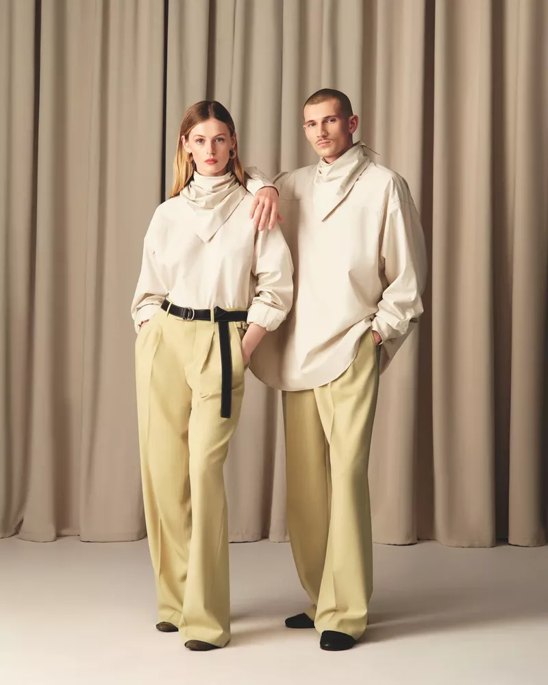 Models Viktoriia Afanasieva and male counterpart posing in loose cream high-neck shirts and pale yellow wide-leg trousers for Ami.