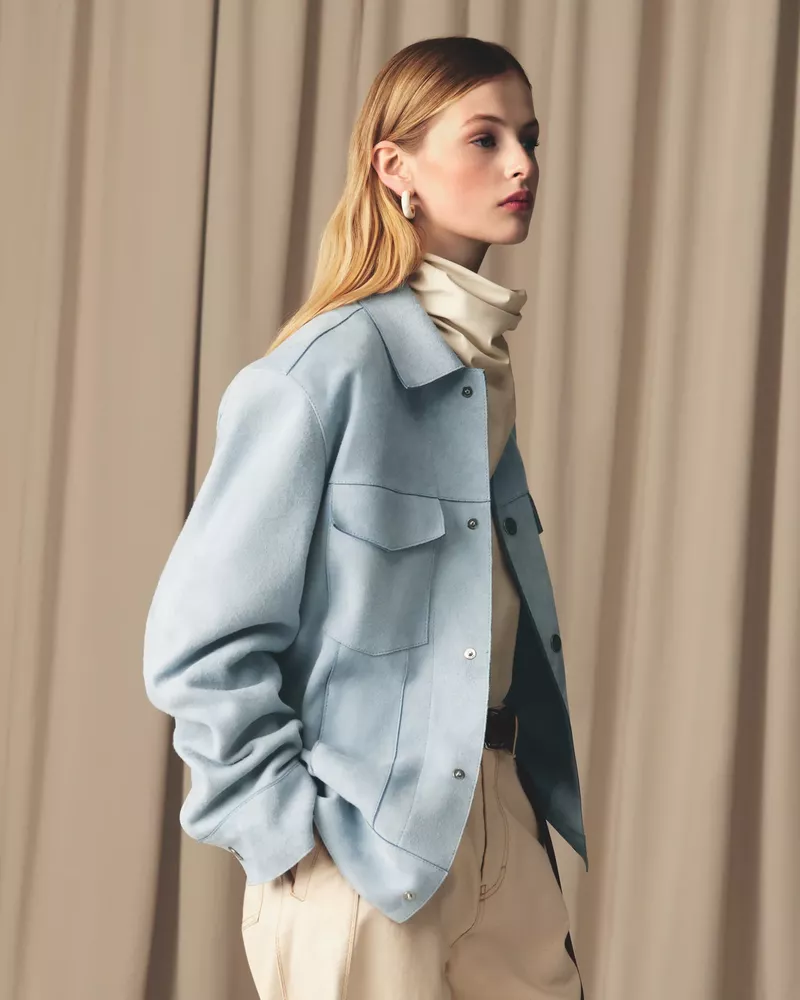 Stylish woman in blue jacket, tan pants posing indoors against neutral backdrop, showcasing fashion and editorial style.