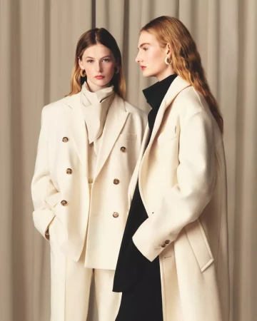 Two female models posing in cream-colored outerwear against a draped curtain background for Ami Stolen Stories.