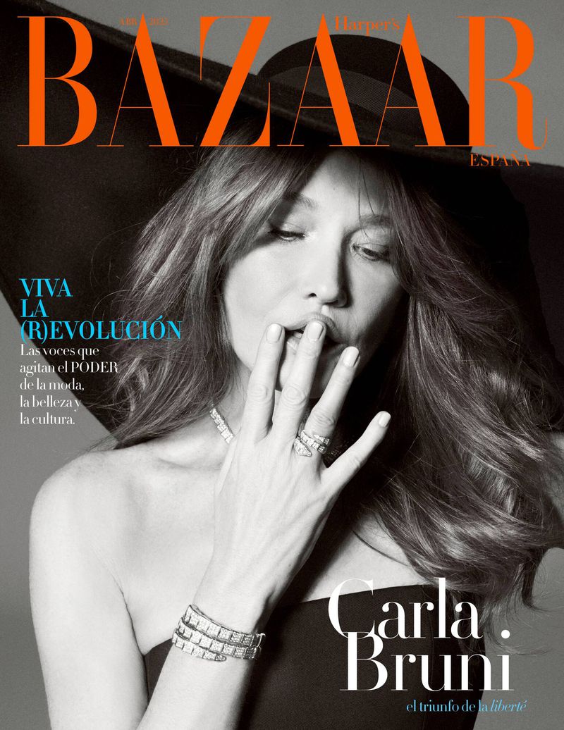 Black and white close-up fashion magazine cover shot of Carla Bruni with her hand near her mouth, wearing jewellery and a black hat.