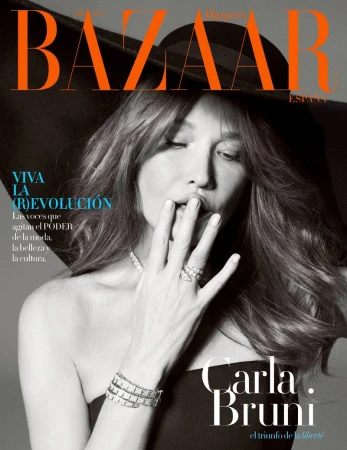 Black and white close-up fashion magazine cover shot of Carla Bruni with her hand near her mouth, wearing jewellery and a black hat.