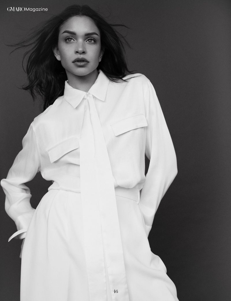 Fashion portrait of a woman in a white blouse and wide-leg pants. The portrait, shot in black and white, shows her posed against a solid backdrop.