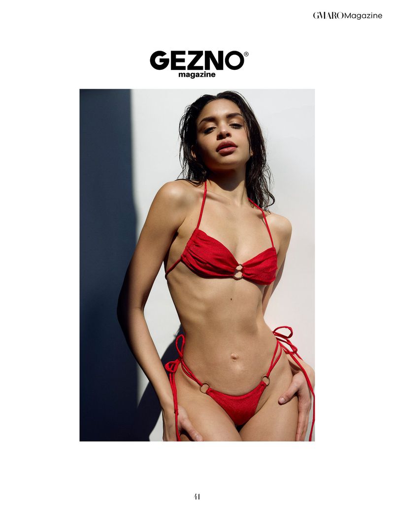 A woman poses in a red bikini, with wet hair, against a textured wall in a fashion editorial style for a magazine cover.