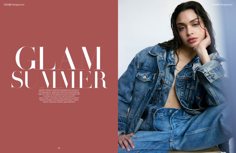 A young woman with wet hair poses while wearing a denim jacket and jeans, seated against a white wall, photographed for GMARO Magazine.