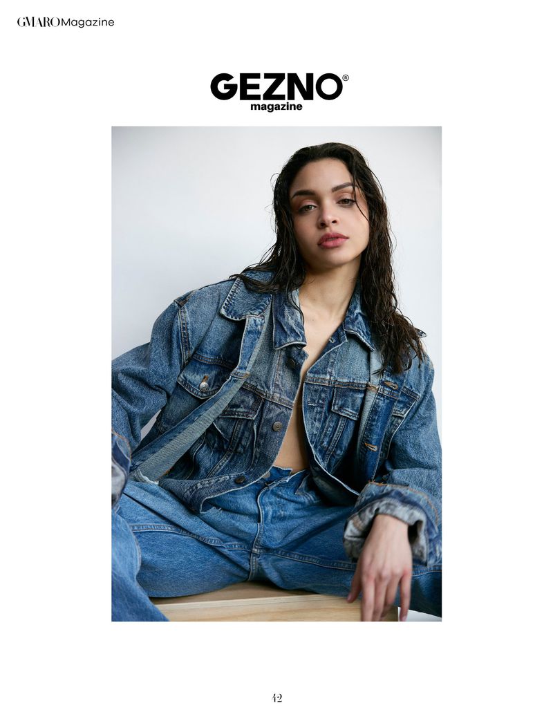 A woman with wet dark hair poses in a denim jacket and jeans in front of a white background for a fashion magazine cover.