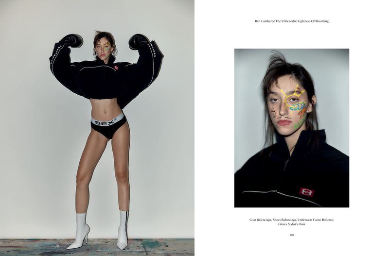 Fashion editorial shot of a slender young woman wearing boxing gloves, briefs, and boots, posing in a photo studio with soft lighting.