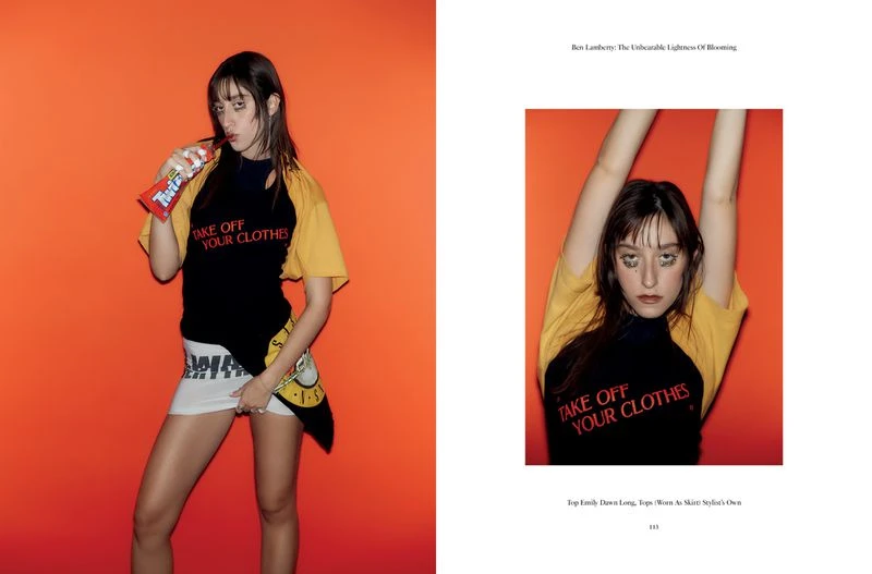 Young adult woman in fashion shot wearing a printed T-shirt with Twizzlers, posing against an orange background in a studio.