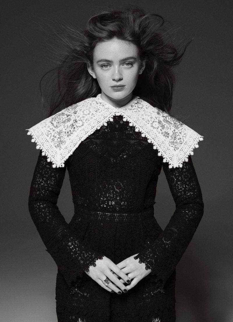 Black and white portrait of a young woman in a black lace dress with a large white lace collar against a plain gray backdrop.