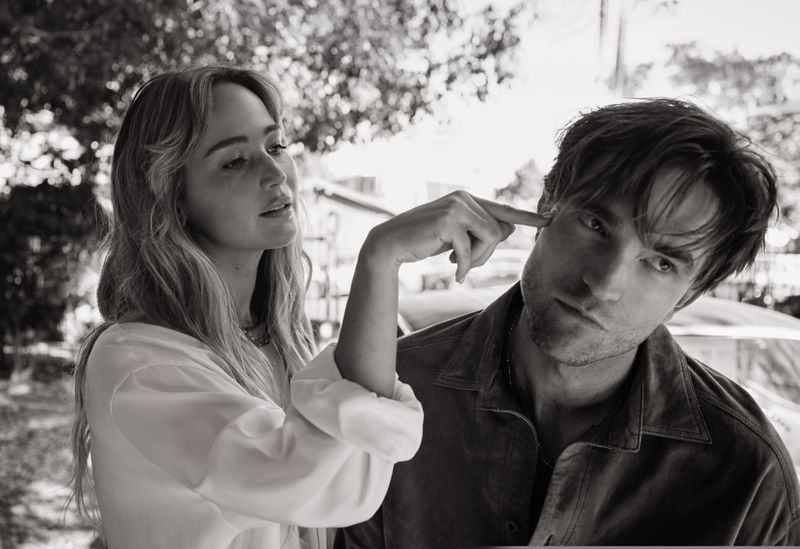 Black and white portrait of a woman touching a man's head with her finger in an outdoor setting with natural lighting.