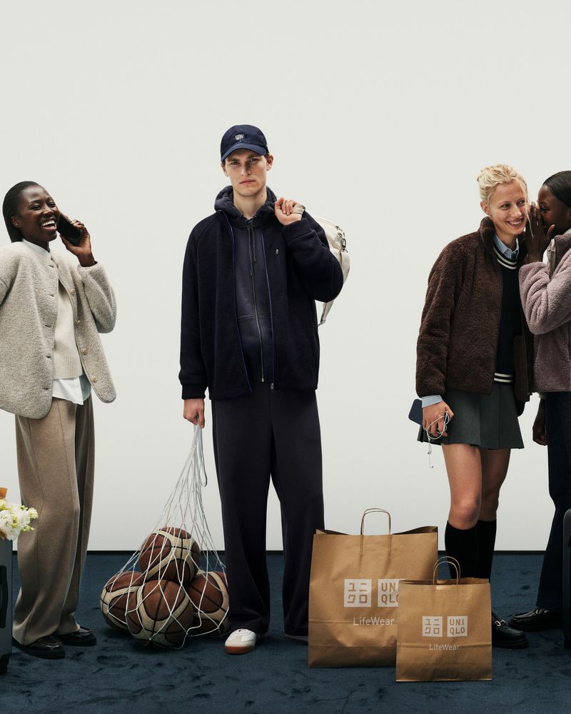 Diverse group of young adults showcase casual apparel with shopping bags against a minimalist backdrop in a fashion editorial.