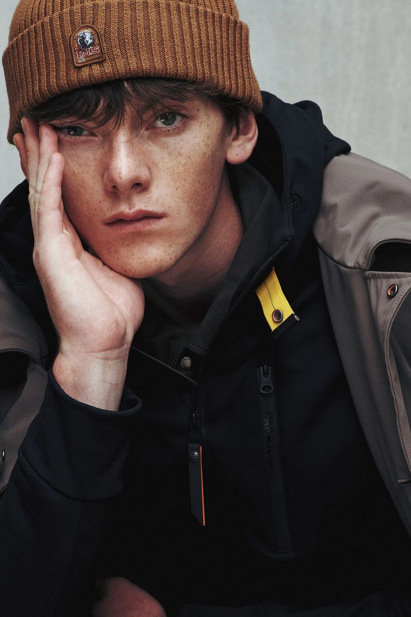 Portrait of a light-skinned adult male with brown hair, wearing a brown beanie and dark jacket, looking at the camera with a serious expression.