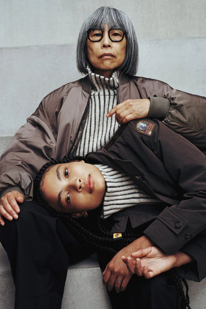 Stylish portrait of an elderly Asian woman with glasses seated, while a young woman with braided hair reclines on her lap.