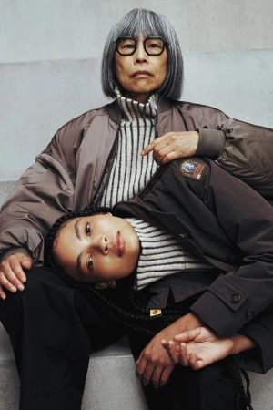 Stylish portrait of an elderly Asian woman with glasses seated, while a young woman with braided hair reclines on her lap.