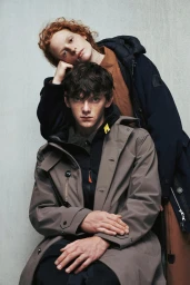 Two models wearing Parajumpers outerwear, including a taupe trench coat and a navy puffer jacket, against a grey studio backdrop.