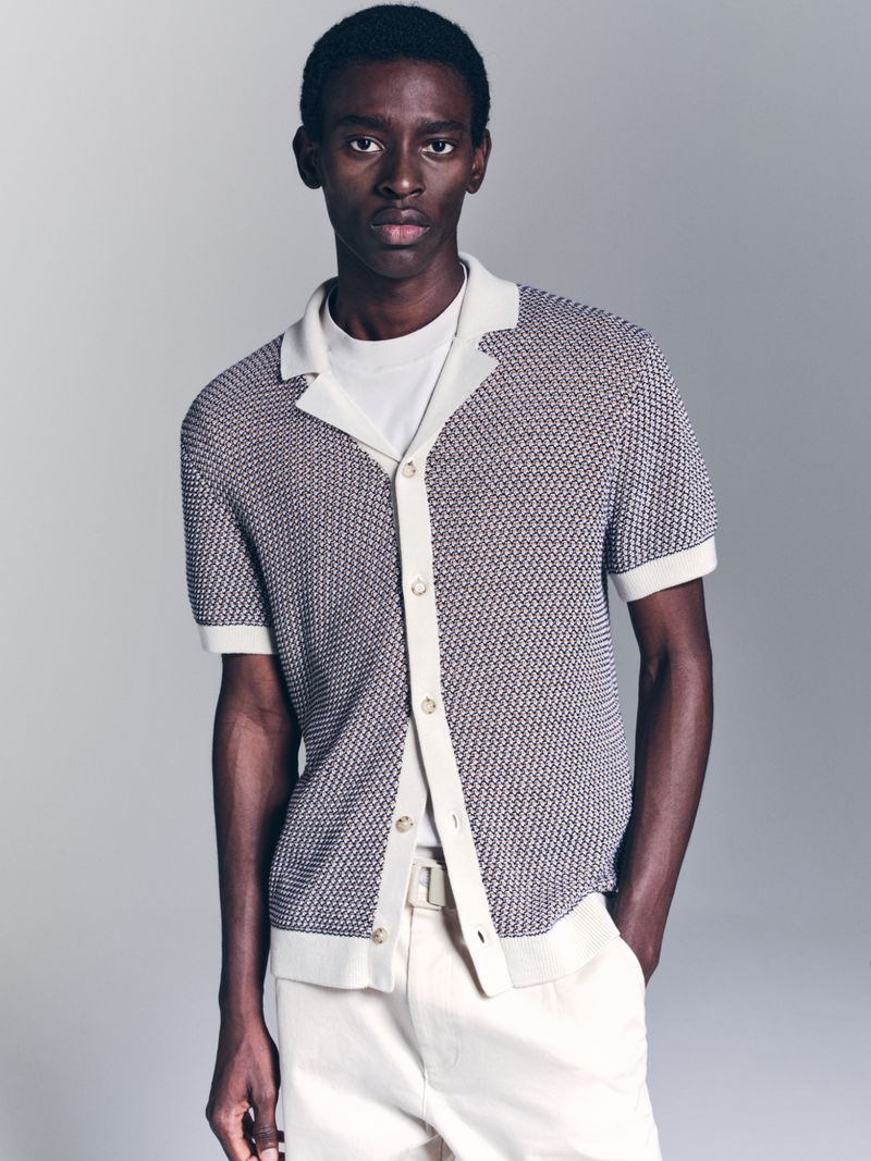 Model Adamu Bulus posing in a textured short-sleeve knit shirt and off-white trousers against a studio backdrop.